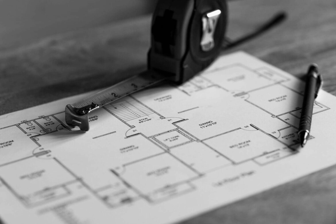 Blueprint, pen, and tape measure on wooden table background.