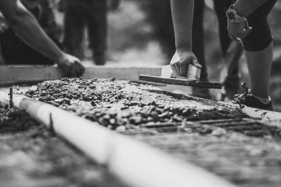 Construction workers laying cement in wooden frame.