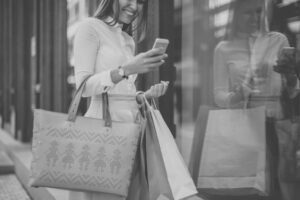 woman holding many shopping bags and smiling at her phone